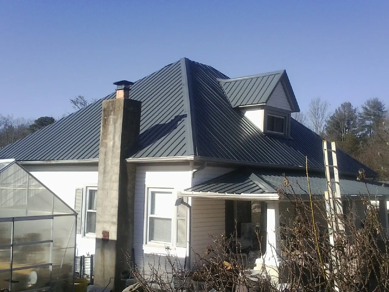 Dark blue standing seam metal roof on a white farmhouse with dormer — Slate & Tile Roof Repair by Roofing Brothers in Cambria