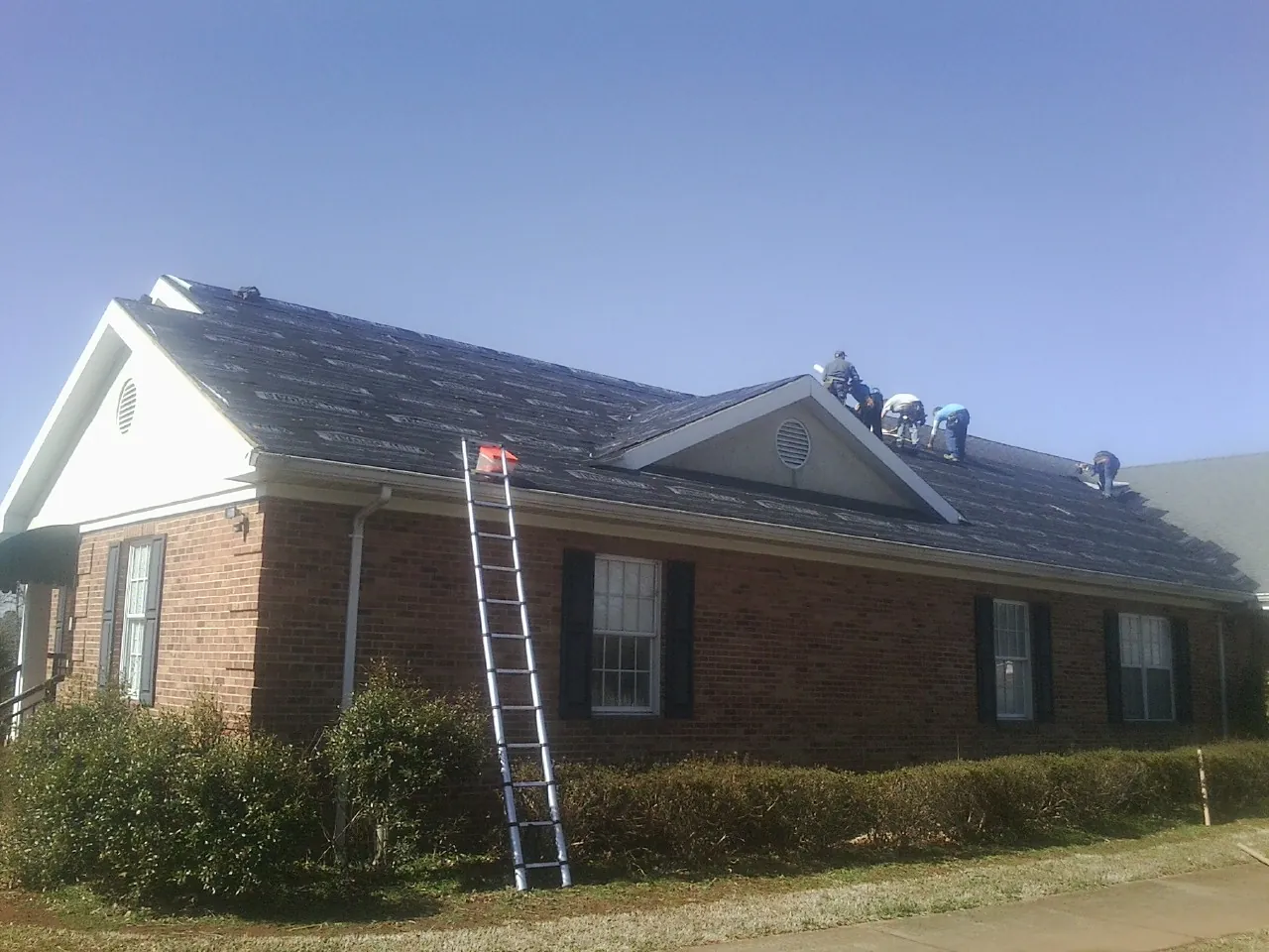Crew tearing shingles off a brick ranch roof with a ladder set — Metal Roof Repair work by our crew in Cambria