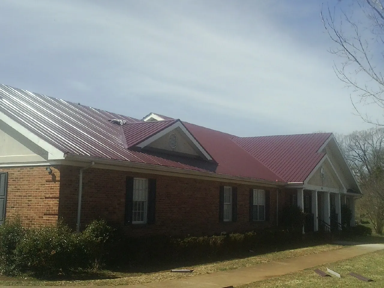 Red metal roof with gabled entries on a long brick building, from a Hail Damage Roof Repair job in Cambria