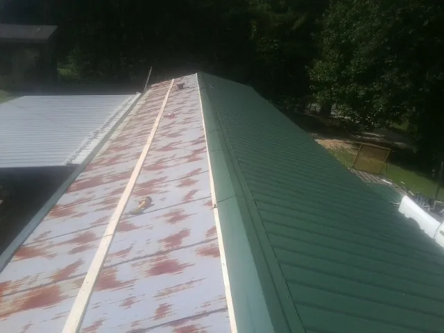 Old rusted panels beside newly installed green metal roofing — Wind Damage Roof Repair by Roofing Brothers in Cambria