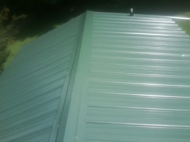 New green metal panels meeting at the ridge of a roof — Flat Roof Repair work by our crew in Cambria