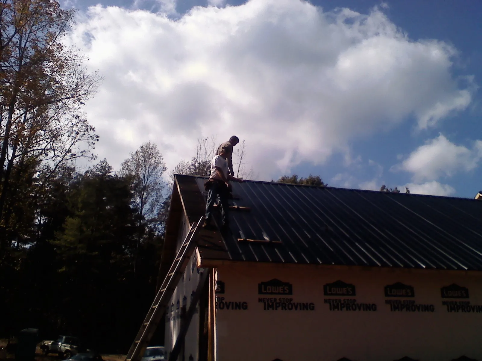 Roofer fastening dark metal panels high against a cloudy sky, from a Roof Inspection job in Cambria