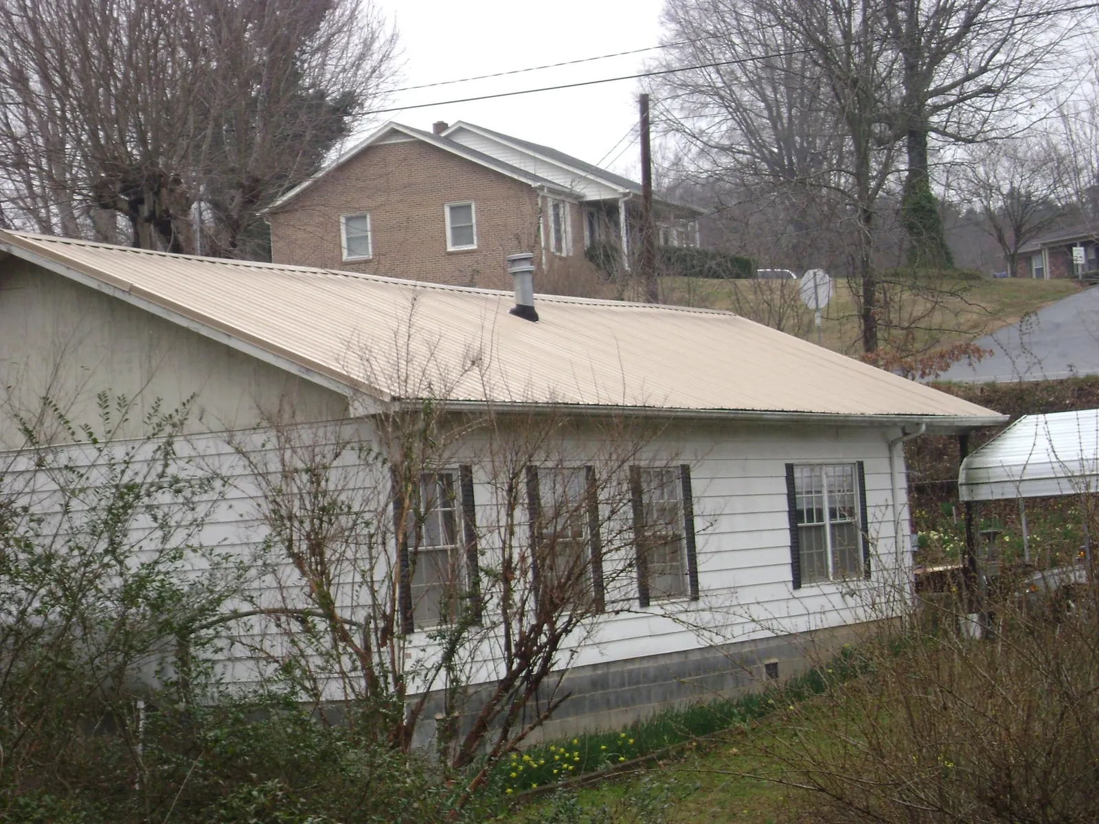Tan metal roof on a white sided house set into a hillside — Commercial Roofing by Roofing Brothers in Cambria